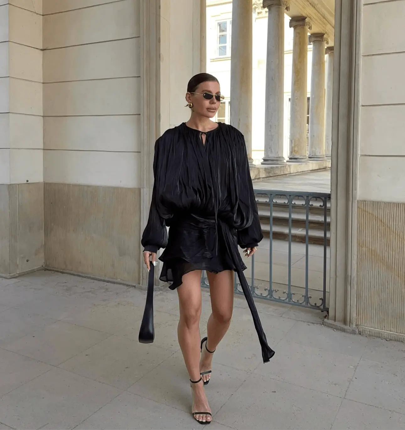 Frau trägt das Éloïse Plissee Kleid in Schwarz mit trendigen Accessoires und elegantem Stil.